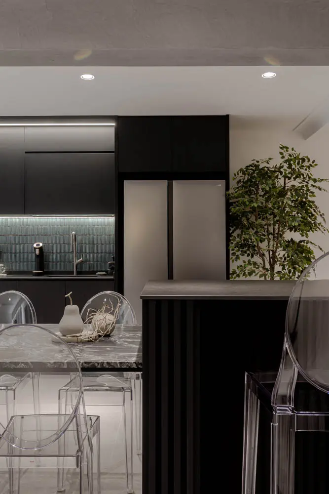 Matte-black kitchen island with sintered-stone counter and ghost chairs